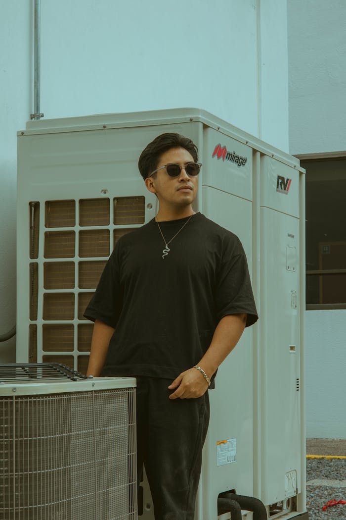 A fashionable man stands confidently near an air conditioning unit, exuding urban style.